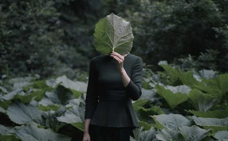 Femme se cachan le visage avec une feuille certainement pour dissimuler ses cernes