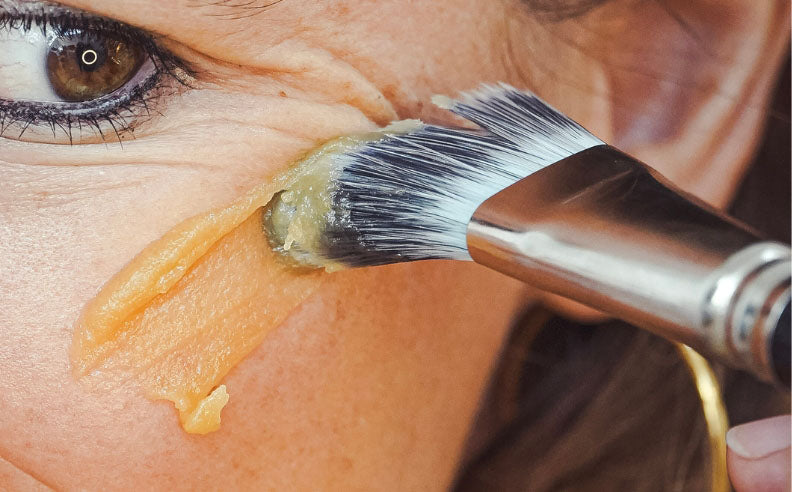 Zoom sur la pommette d'une femme qui s'applique le masque réparateur au miel